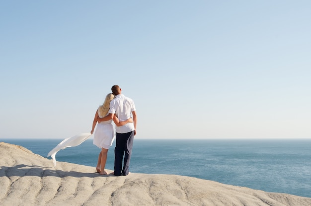 Homme et femme debout bras dessus bras dessous sur un rocher et regarder la mer