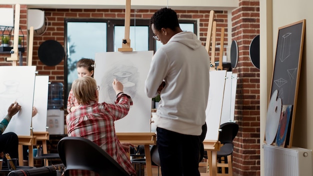 Homme et femme donnant des conseils à un étudiant plus âgé en classe d'art, dessinant un modèle de vase sur toile pour développer des compétences artistiques. Apprendre à dessiner des croquis avec des instruments et des outils de croissance. Prise de vue au trépied