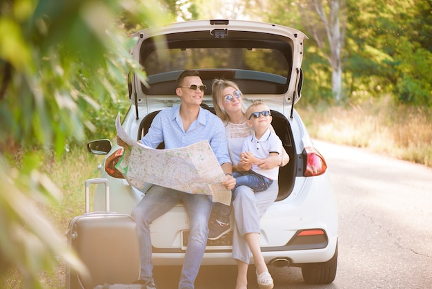 Un homme, une femme et un enfant de quatre ans dans les bois à côté de la voiture est prêt à voyager et à choisir un endroit sur la carte où aller.