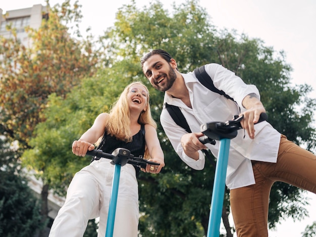 Photo homme et femme à faible angle à l'aide de scooters à l'extérieur