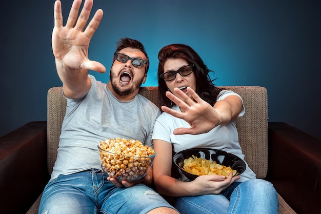 Un homme et une femme, une famille regardant un film ou une série de lunettes 3D, un mur bleu. Le concept de cinéma, films, émotions, surprise, loisirs, plateformes de streaming.