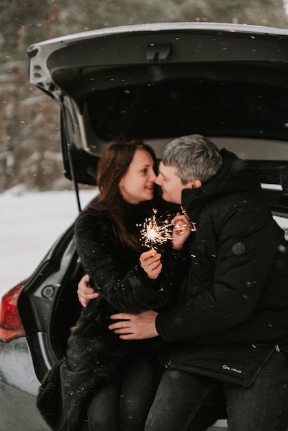 Un homme et une femme sur le fond d'une forêt couverte de neige dans une chute de neige dans le coffre d'une voiture