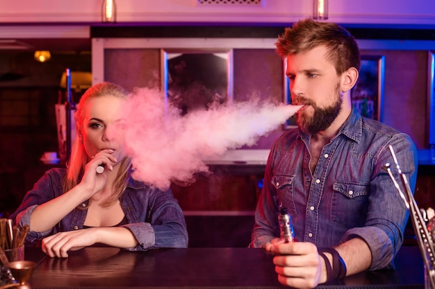 Un homme et une femme fumant une cigarette électronique dans un bar à vapeur.