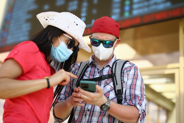 Homme et femme à la gare dans des masques médicaux de protection sont à la recherche de smartphon