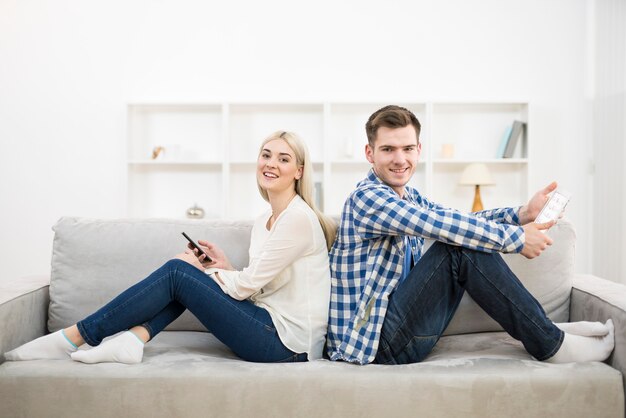 L'homme et la femme heureux avec un téléphone et une tablette sont assis sur le canapé