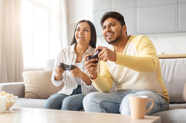 Un homme et une femme indiens jouent à un jeu vidéo sur le canapé.