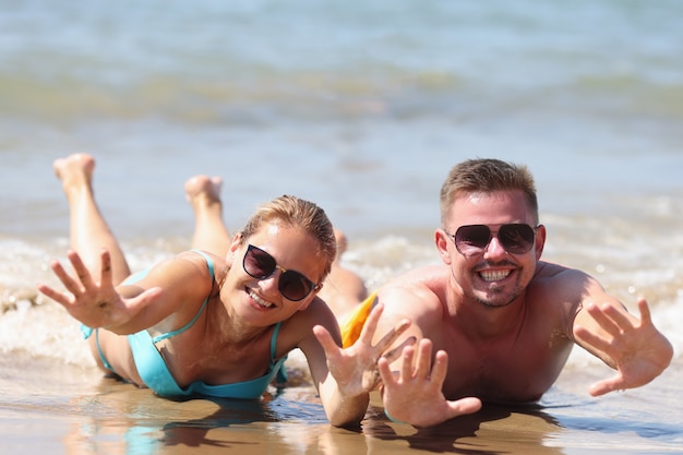 L'homme et la femme joyeux dans des lunettes de soleil se trouvent sur le sable humide près de la mer