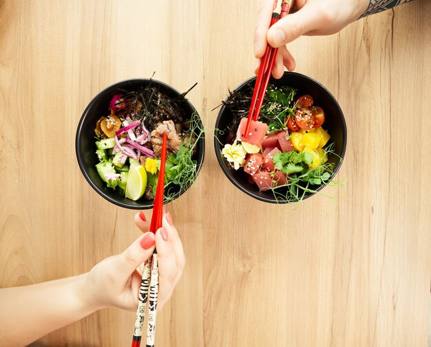 Homme et femme mangeant de la salade de poke avec des baguettes. Tamponnez la salade de thon dans un bol. Les gens dans le restaurant mangent de la salade avec des baguettes. Concept de salade de fruits de mer asiatique.