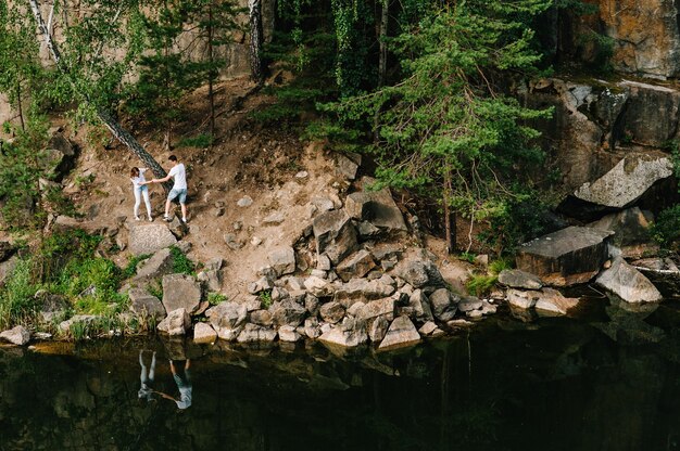 Un homme et une femme marchent le long des rochers, rampent sous l'arbre, près de la forêt et du lac