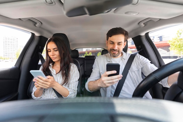 Homme et femme millénaires assis à l’intérieur d’une voiture à l’aide de smartphones