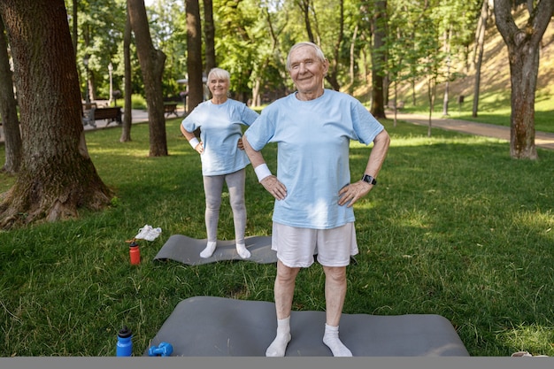 Homme et femme mûrs sportifs s'entraînent sur des tapis sur une pelouse luxuriante