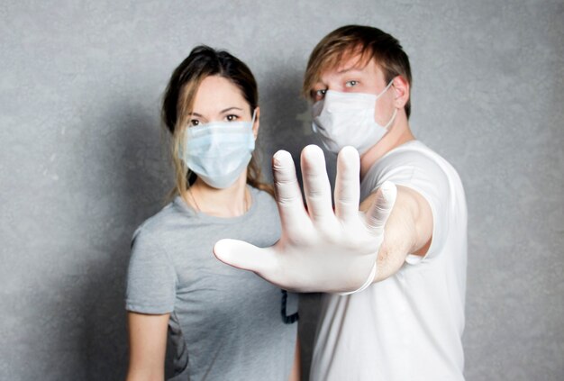 Un homme et une femme portant des masques et des gants montrent un arrêt Un homme portant un masque médical montre un geste de la main