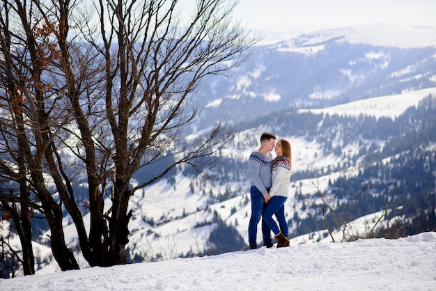 Homme et femme portant des vêtements tricotés s'embrassant sur la montagne enneigée.