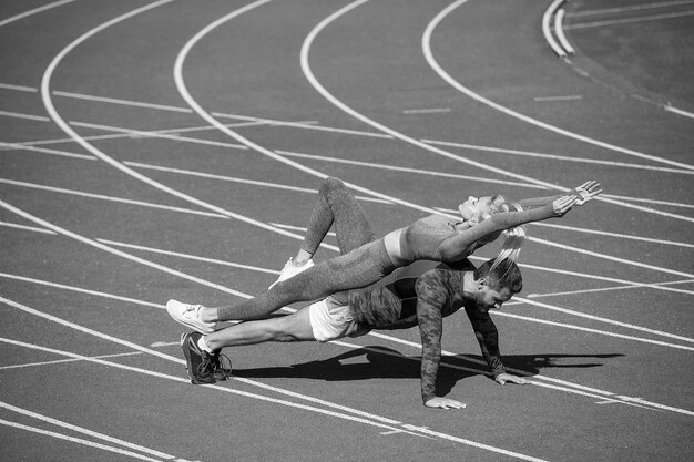 Un homme et une femme de remise en forme sportive s'entraînant ensemble se tiennent en planche et poussent sur l'hippodrome du stade en plein air portant des vêtements de sport