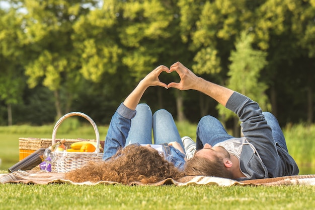 L'homme et la femme s'allongent sur l'herbe et font un geste symbole d'amour