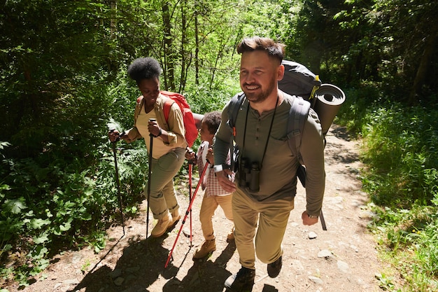 Homme et femme avec des sacs à dos marchant le long du chemin dans la forêt avec leur fils, ils vont camper