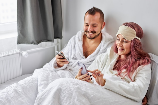 L'homme et la femme se reposent avec un téléphone mobile sur le lit