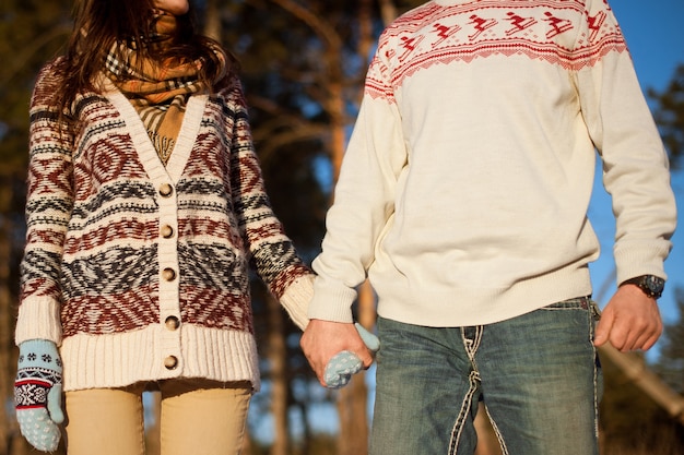 Homme et femme se tenant la main dans des chandails d'hiver à la surface des pins