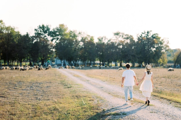 Un homme et une femme se tenant la main marchent le long d'une route de campagne