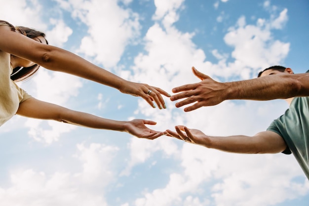 Un homme et une femme se tendent la main et se touchent les doigts sur un fond de ciel bleu.