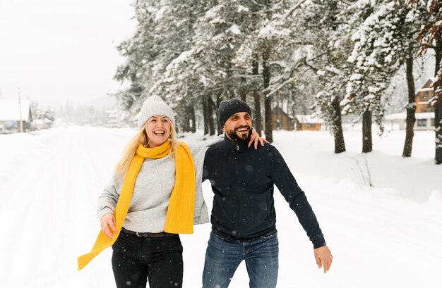 Homme et femme séduisants se blottissant dans la forêt givrée. Un couple adulte en chandail s'amuse en marchant. Rendez-vous romantique en hiver. Histoire d'amour d'hiver