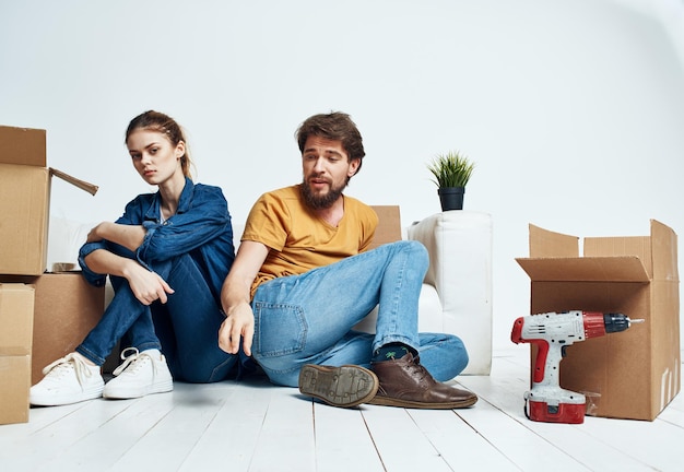 Un homme et une femme sont assis sur le sol à l'intérieur près du canapé et des boîtes de déménagement