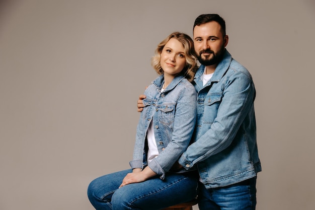 Un homme et une femme sont assis sur un tabouret, portant des vestes en jean et une chemise blanche.