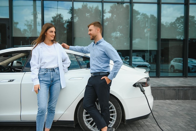 Homme et femme souriants sur la borne de recharge pour voitures électriques Un homme charge une voiture