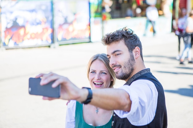 Photo un homme et une femme souriants se font un selfie alors qu'ils se tiennent dans la rue lors d'un événement.