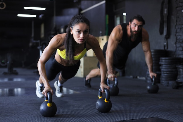 Homme et femme sportifs faisant des pompes dans une salle de sport.