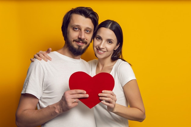 Un homme et une femme en T-shirts blancs tiennent un cœur en papier le jour de la Saint-Valentin