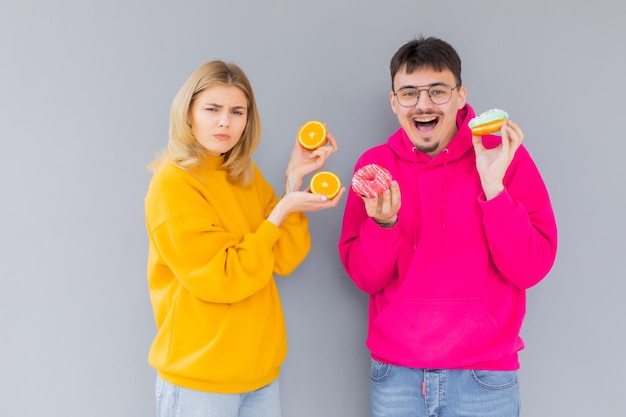 Homme et femme tenant des beignets et orange sur fond gris Concept de mode de vie sain