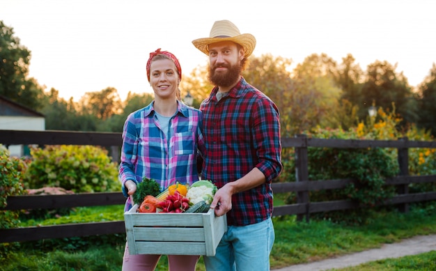 Un homme et une femme tenant une boîte avec une récolte de légumes de la ferme