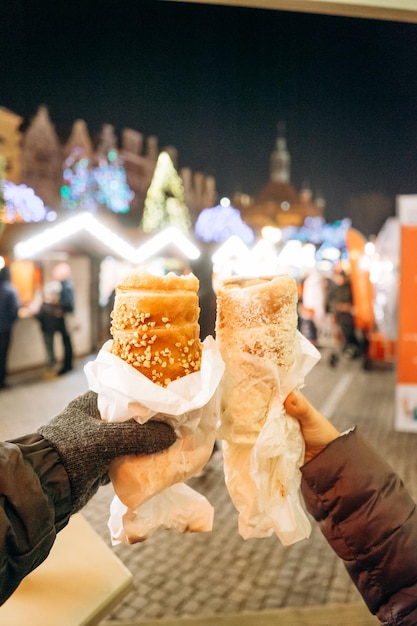 Homme et femme tenant un rouleau polonais traditionnel sucré Dessert au chocolat sur fond du marché de Noël de la ville européenne Nourriture de rue traditionnelle sucrée en Pologne