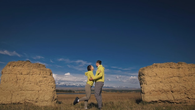 Homme et femme en tenue de sport vert jaune. Un charmant couple de voyageurs s'embrasse et s'embrasse près de la vieille pierre en profitant du paysage des hautes terres. Deux voyageurs marchent sur fond de montagnes enneigées.