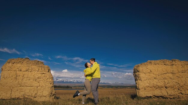 Homme et femme en tenue de sport vert jaune. Un charmant couple de voyageurs s'embrasse et s'embrasse près de la vieille pierre en profitant du paysage des hautes terres.