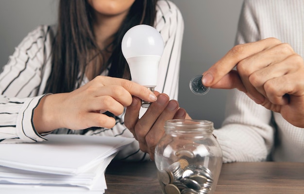 Un homme et une femme tiennent une ampoule et jettent une pièce de monnaie dans une tirelire