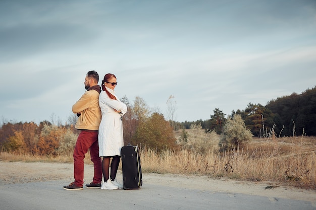 Homme et femme voyageant avec une valise sur une route vide