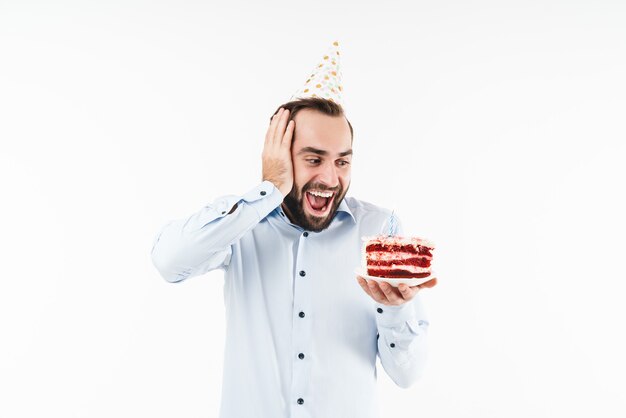 homme de fête étonné souriant et tenant un gâteau d'anniversaire avec une bougie isolé sur un mur blanc