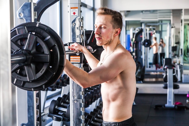 Un homme de fitness déterminé et fort se prépare à s'entraîner avec des poids lourds dans un club de fitness. Athlète séduisant d'homme musclé travaillant avec des haltères lourds dans une salle de sport.