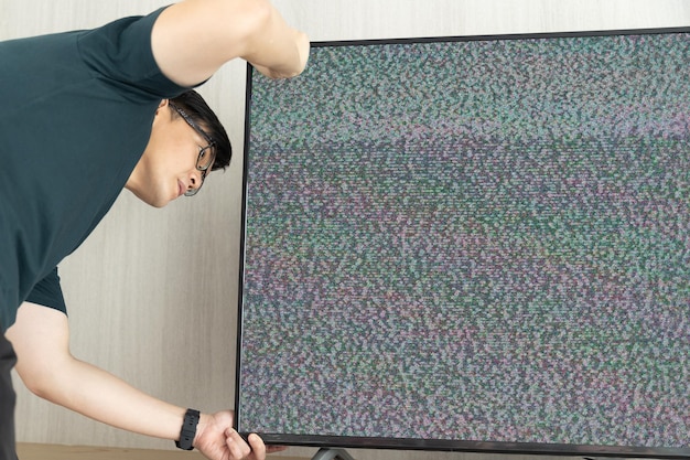 Un homme fixe le bruit du signal perdu de la télévision à l'écran en regardant le câble derrière