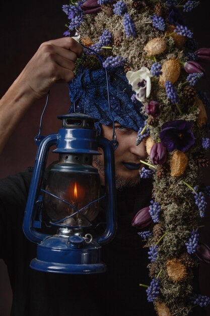 Un homme avec des fleurs bleues et une lampe sur une pièce sombre