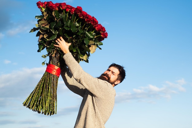 Homme avec des fleurs roses un homme heureux tient un gros bouquet de roses rouges propose à son petit ami le jour de la rom