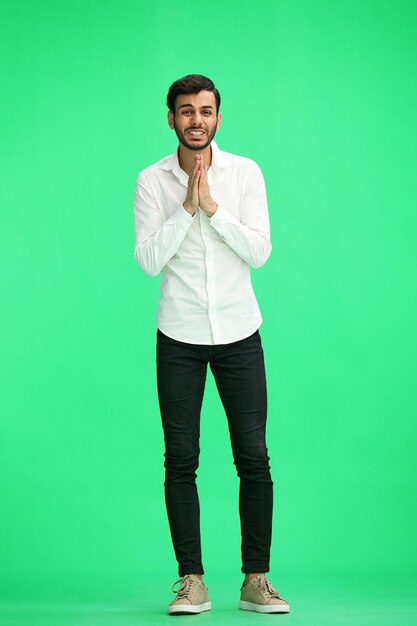 un homme sur un fond vert en pleine hauteur tient ses mains ensemble