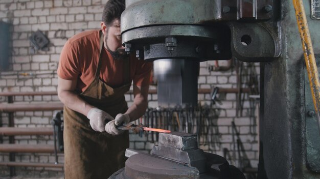 Homme forgeron en atelier forgeant du fer rouge sur l'enclume - petite entreprise, téléobjectif