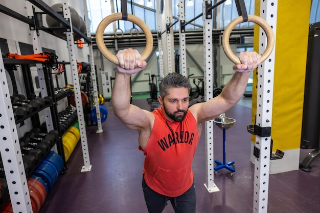 Un homme en forme adulte barbu s'entraîne sur des anneaux de gymnastique dans un entraînement de gymnastique en entraînant ses biceps et ses triceps