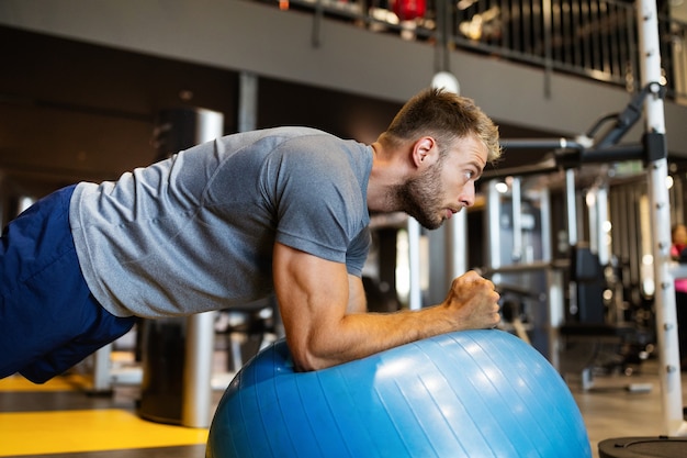 Homme en forme heureux faisant des exercices de remise en forme sur ballon de pilates dans une salle de sport