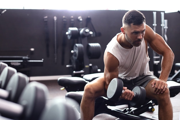 Homme en forme et musclé faisant des exercices de biceps avec des haltères dans une salle de sport, copiez l'espace.