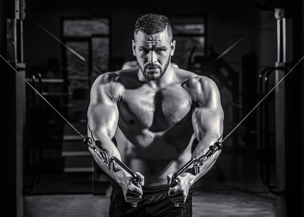 L'homme De Forme Physique Exécute L'exercice Avec Le Croisement De Câble D'exercice-machine Dans Le Gymnase. Bel Homme Avec De Gros Muscles Dans La Salle De Gym. Machine Dans La Salle De Gym. Noir Et Blanc.