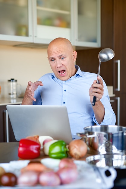 Homme fort adulte dans la cuisine, préparer la nourriture et se penche sur l'ordinateur portable